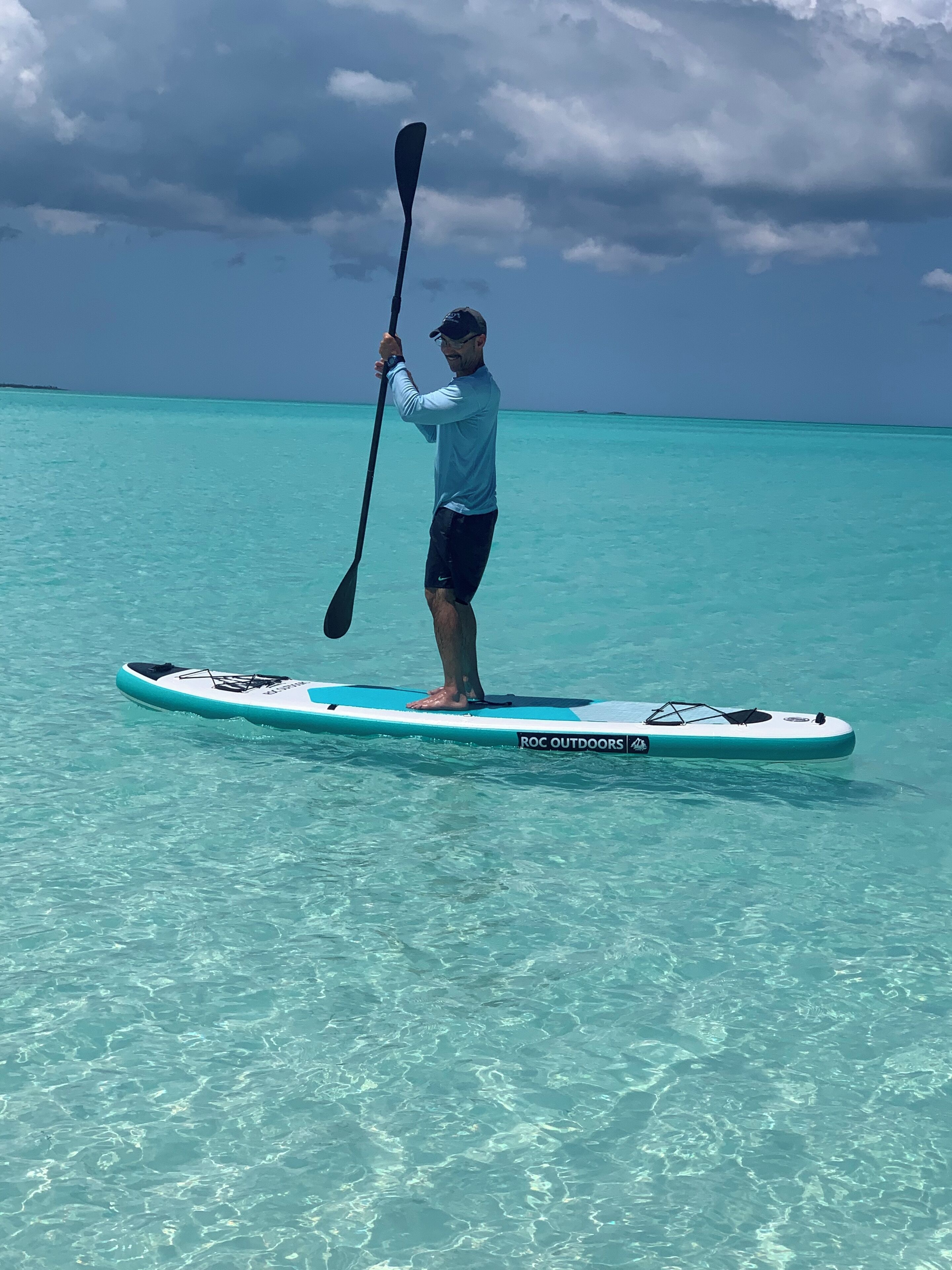 A person standing on a paddleboard in clear turquoise water.