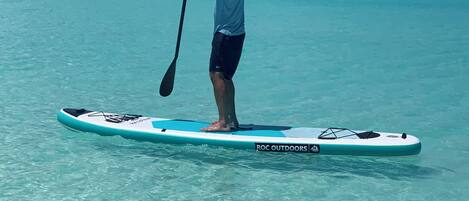 A person standing on a paddleboard in clear turquoise water.