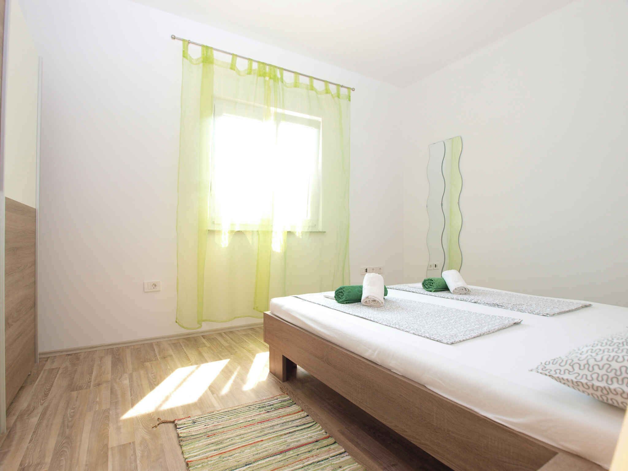 Un dormitorio con cama, espejo, ventana con cortinas traslúcidas y una alfombra a rayas.
