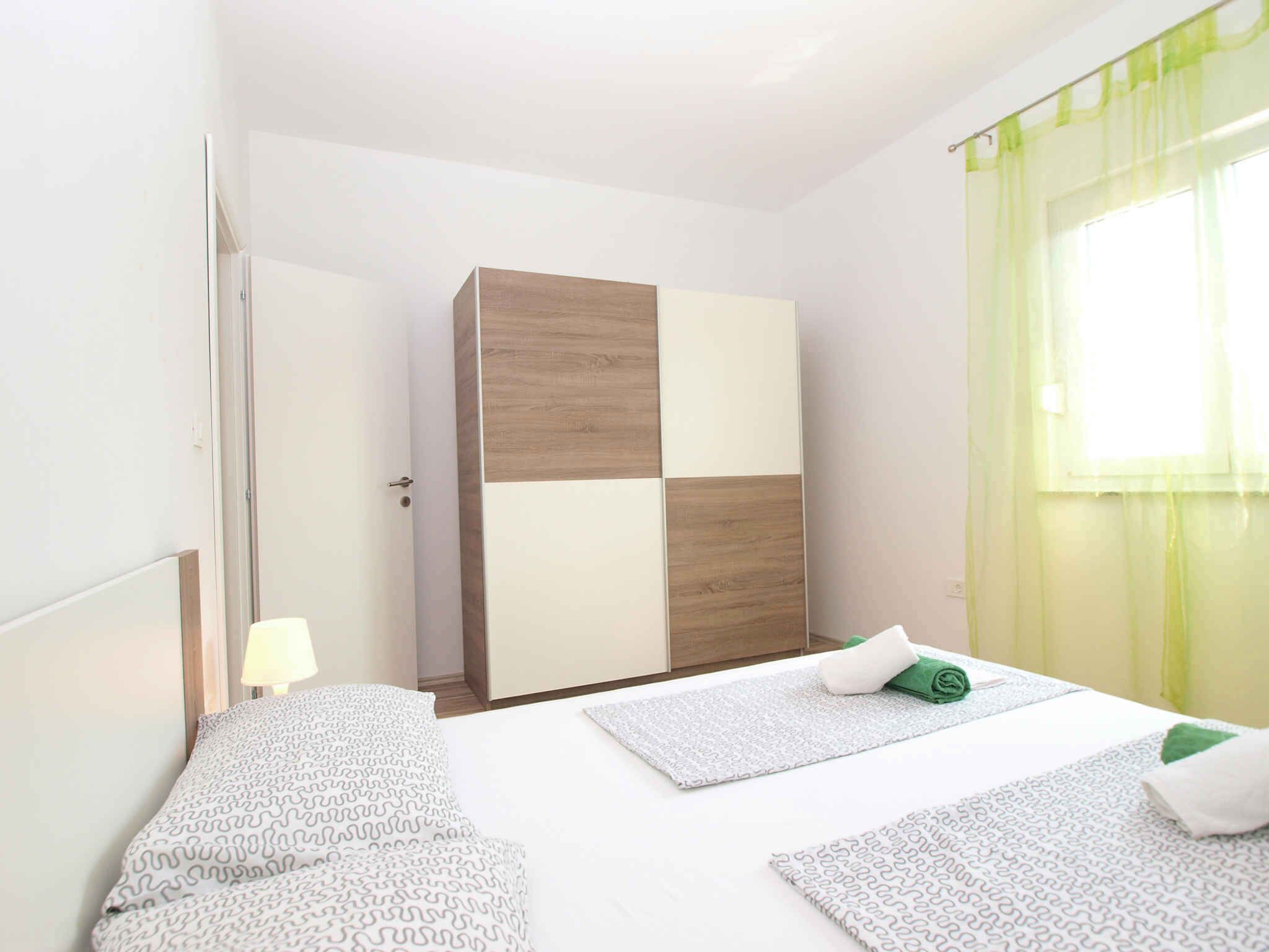 Una habitación de hotel con cama, armario, mesita de noche y ventana con cortinas.