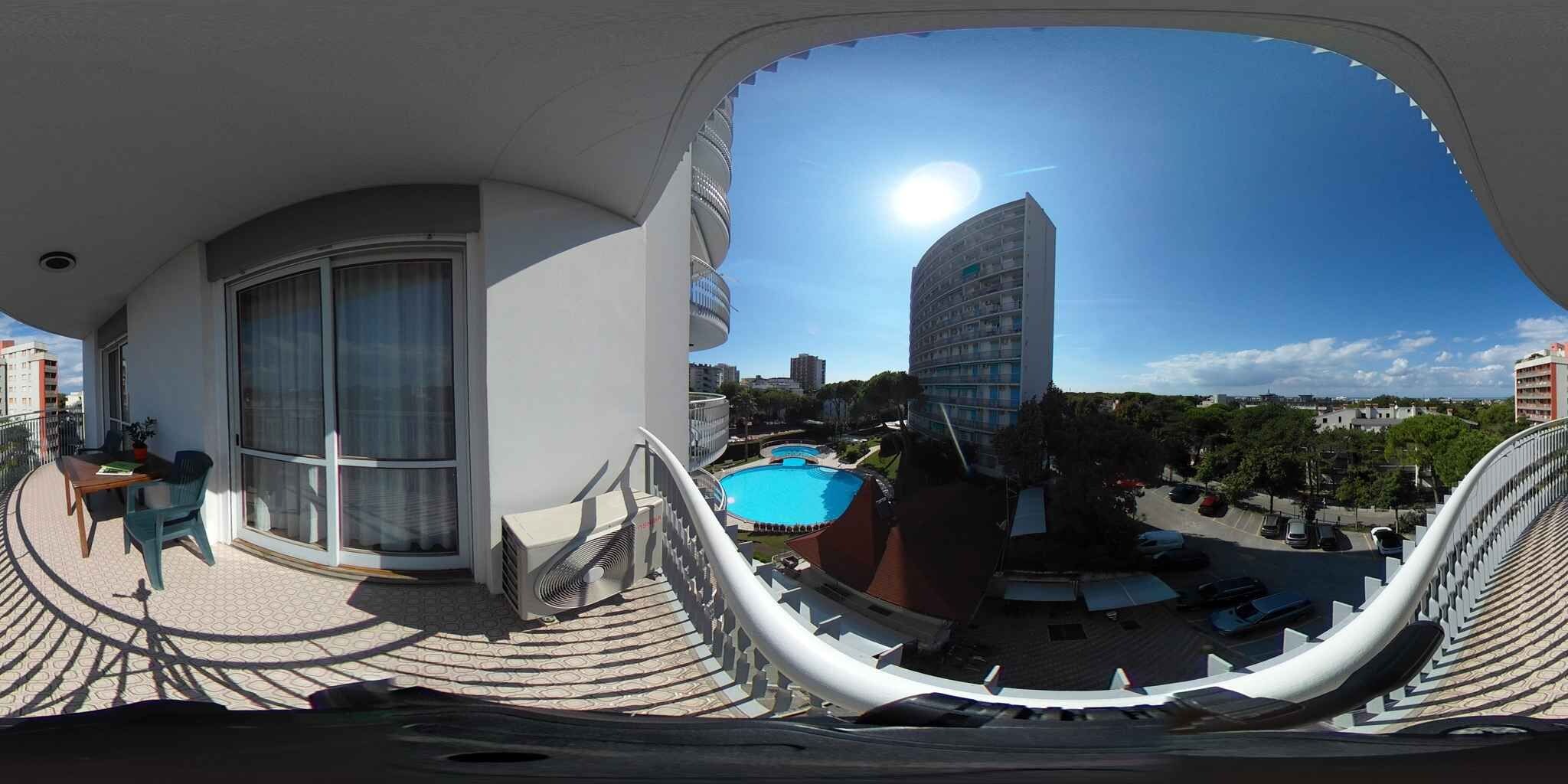 Een balkon met uitzicht op een zwembad, een hoog gebouw en een heldere lucht.