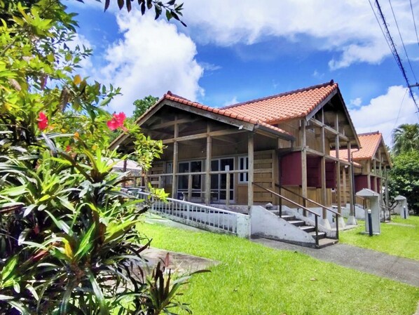 Une maison en bois à deux étages, avec un toit recouvert de tuiles rouges, une véranda et un escalier menant à l’étage supérieur.