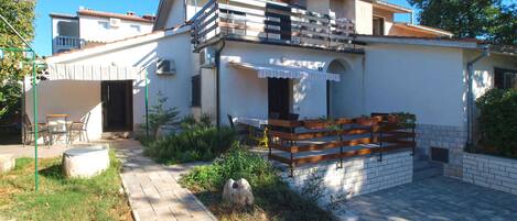 Una casa de dos pisos con un balcón, un patio con mobiliario exterior y un jardín.