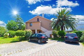 Una casa de dos pisos con entrada pavimentada y coches aparcados.
