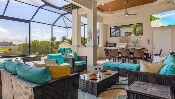 A spacious outdoor area with wicker furniture, a dining table, and a large TV screen. - Gulf Access, Putting Green, Outdoor Kitchen, Heated Pool & Spa & MORE! - Villa Captain's Quarters (Cape Coral)