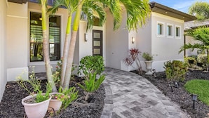 A modern house with a paved walkway, potted plants, and a door with a window above it. - Gulf Access, Putting Green, Outdoor Kitchen, Heated Pool & Spa & MORE! - Villa Captain's Quarters (Cape Coral)