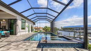 A swimming pool with a glass ceiling, a view of a body of water, and a patio area with seating. - Gulf Access, Putting Green, Outdoor Kitchen, Heated Pool & Spa & MORE! - Villa Captain's Quarters (Cape Coral)