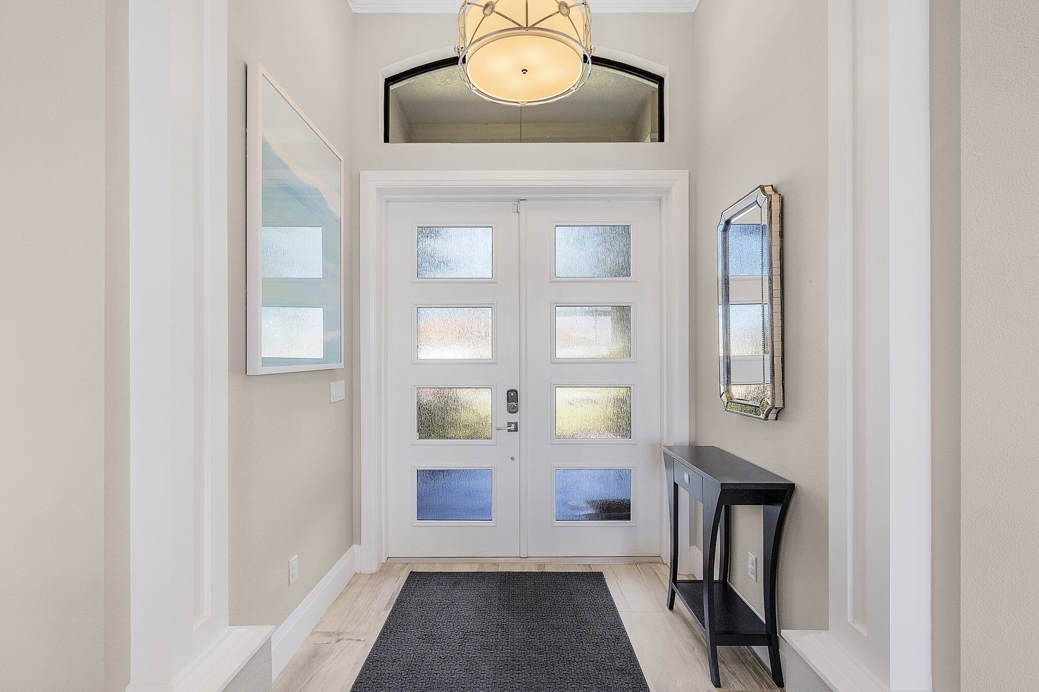 Un couloir avec une porte à deux battants, une console et un miroir au mur.
