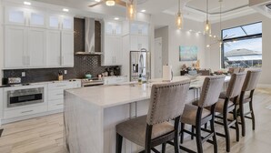A modern kitchen with white cabinets, a large island, and bar stools. - Gulf Access, Putting Green, Outdoor Kitchen, Heated Pool & Spa & MORE! - Villa Captain's Quarters (Cape Coral)