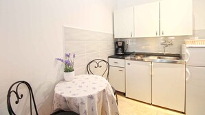 A compact kitchen with white cabinets, a coffee maker, and a small dining table with a floral tablecloth. - Holiday apartment with air conditioning (Fažana)