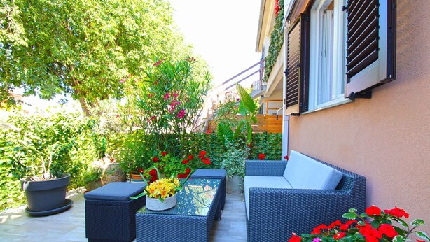 An outdoor patio with wicker furniture, potted plants, and a view of a building. - Holiday apartment with air conditioning (Fažana)