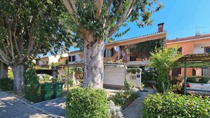A residential area with a tree-lined street, a parked car, and a building with a balcony. - Holiday apartment with air conditioning (Fažana)