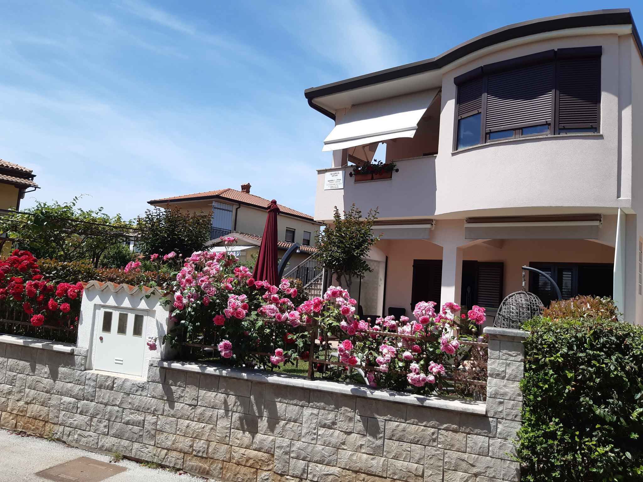 A two-story house with a stone wall and a garden with pink flowers.