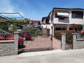 A gated residential area with a red car parked in front, a staircase leading to a building, and a clear sky. - Holiday apartment with air conditioning (Novigrad)
