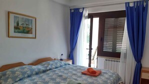 A bedroom with a bed, a nightstand, a lamp, a window with curtains, and a painting on the wall. - Holiday apartment with air conditioning (Novigrad)