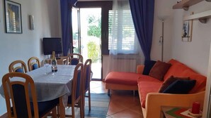 A dining area with a table set for four, a sofa, and a TV on the wall. - Holiday apartment with air conditioning (Novigrad)