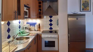 A compact kitchen with wooden cabinets, a stainless steel refrigerator, a microwave, a stove, and a sink with a dish rack. - Holiday apartment with air conditioning (Novigrad)