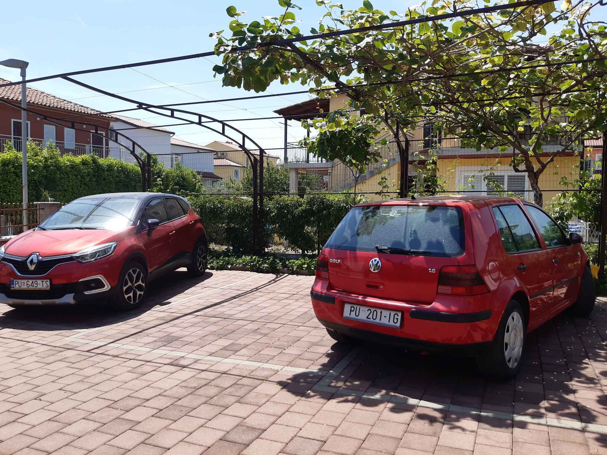 Two red cars parked in a driveway with a tiled surface, surrounded by greenery and residential buildings.