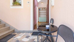 A small outdoor seating area with a table and chairs, a window with a plant, and a staircase leading to an interior space. - Holiday apartment with air conditioning (Novigrad)