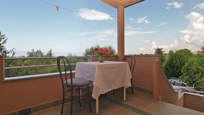 A balcony with a table and chairs, a vase with flowers, and a clear view of the sky and greenery. - Studio with sea view and air conditioning (Peroj)