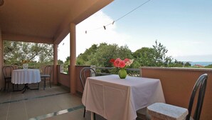 A covered outdoor seating area with a table and chairs, a vase with flowers, and a view of trees and the sea. - Studio with sea view and air conditioning (Peroj)