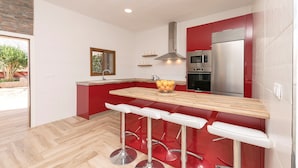 A modern kitchen with red cabinetry, a wooden countertop, and three white bar stools. - CASA ROJA - Lovely villa with private pool (Vejer de la Frontera)