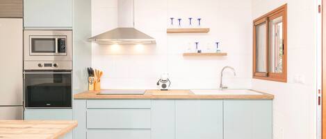 Een moderne keuken met lichtblauwe kasten, roestvrijstalen apparatuur en houten aanrechtbladen.