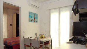 A compact kitchen with a dining area, a bed with a colorful bedspread, and a painting on the wall. - Holiday apartment mjit balcony (Bibione)