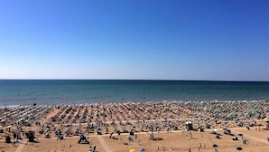 A crowded beach with numerous umbrellas and sun loungers, indicating a busy tourist spot. - Holiday apartment mjit balcony (Bibione)