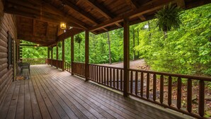 Una terraza de madera con barandilla, bancos y vista a un bosque.
