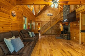 Ein rustikales Blockhaus-Interieur mit einer Holztreppe, einem Kamin und einer Couch mit Kissen.