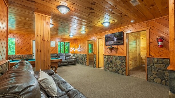 Un interior de madera con un sofá de cuero, mesa de billar, televisor y detalles de piedra.