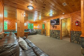 A wooden interior with a leather couch, a pool table, a television, and stone accents.