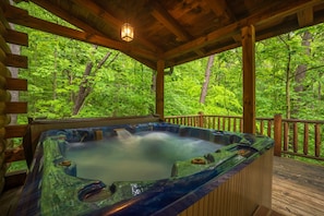 A hot tub on a wooden deck with a forest view.