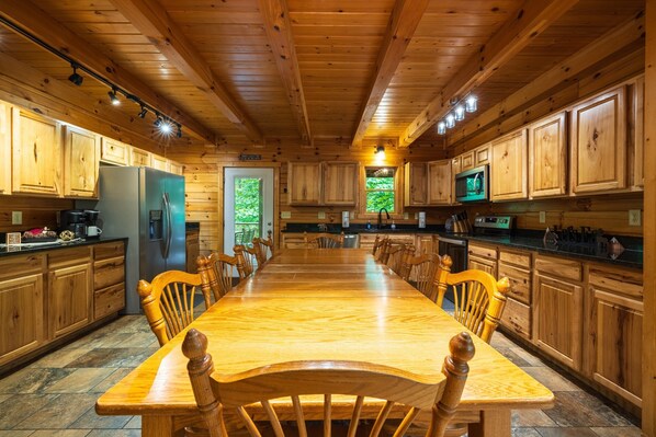A wooden cabin interior with a long dining table, wooden cabinets, and a large window.
