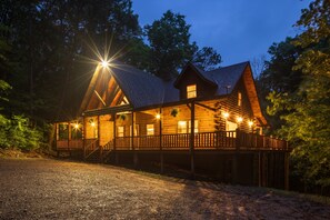A wooden cabin with a porch, multiple windows, and a gravel driveway.