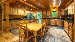 Interior de una cabaña de madera con una mesa de comedor, sillas, armarios y una zona de cocina.