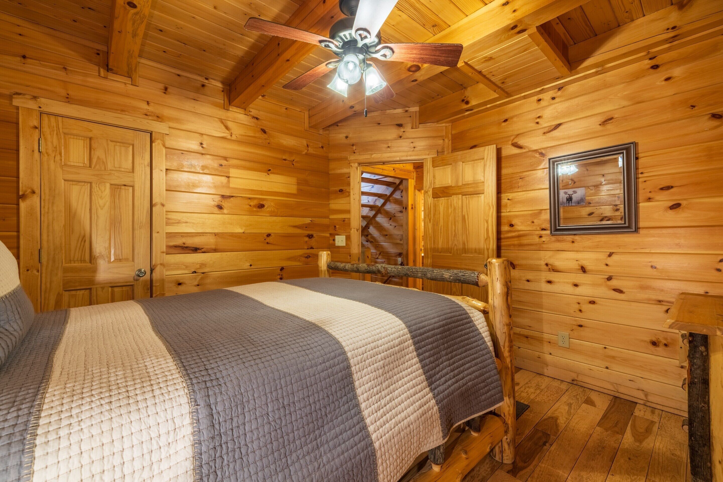 Habitació d'una cabana de fusta amb un llit, un ventilador de sostre i un quadre a la paret.