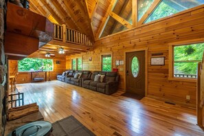 A wooden cabin interior with a sofa, wooden floors, and large windows.