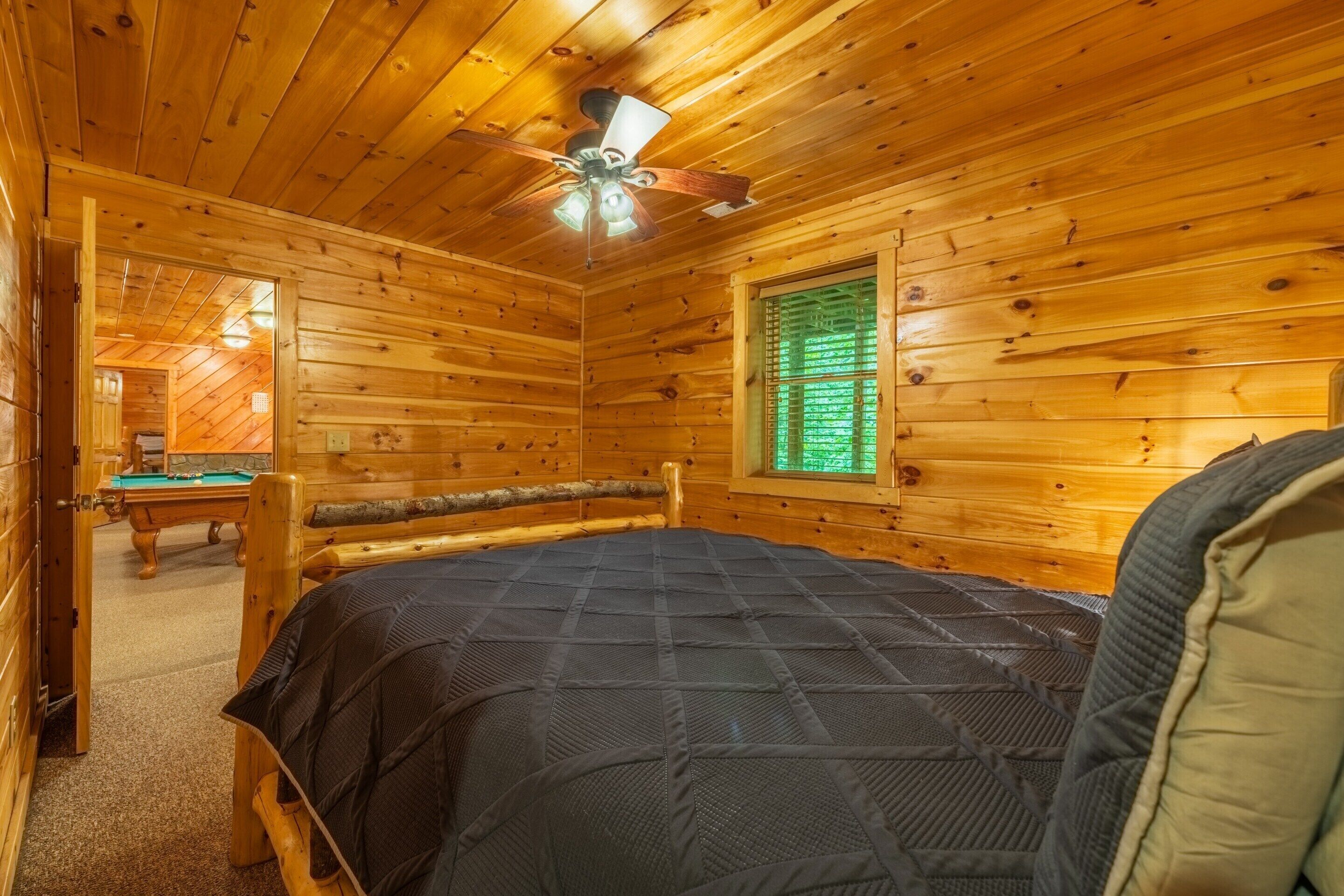 Una baita di legno con un letto, una ventola a soffitto, una finestra con persiane e un tavolo da biliardo.