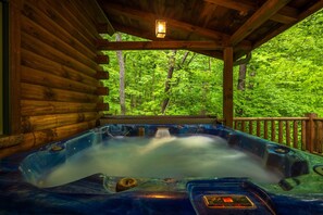 Una cabaña de madera con un jacuzzi y vistas a un bosque.