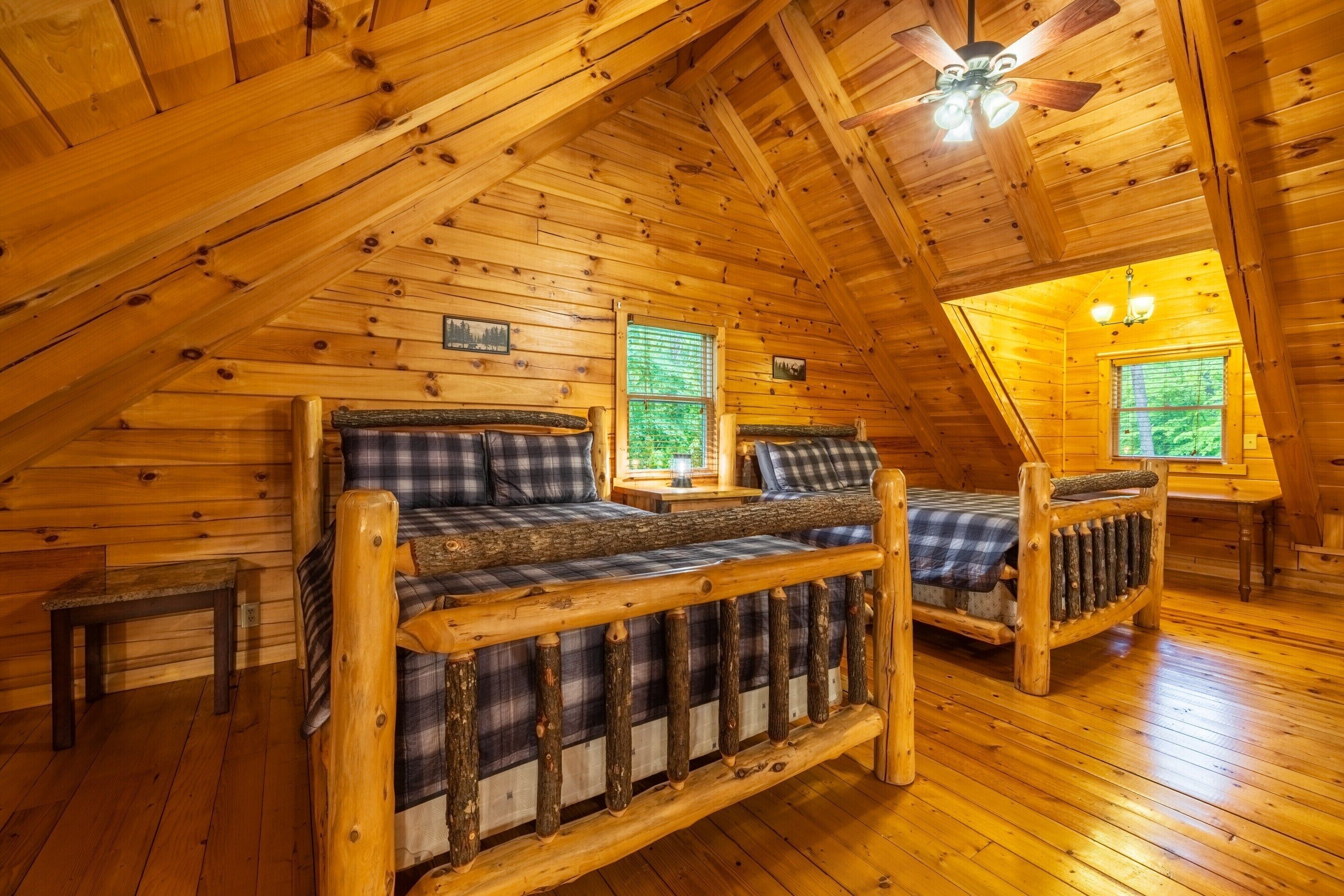 A log cabin interior with a loft bedroom, wooden floors, and a ceiling fan.