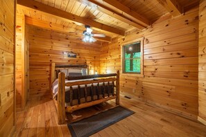 Habitación de cabaña de madera con una cama, un ventilador de techo y una ventana con persianas.
