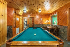 A pool table with a white ball in the center, surrounded by wooden walls and a stone accent wall.