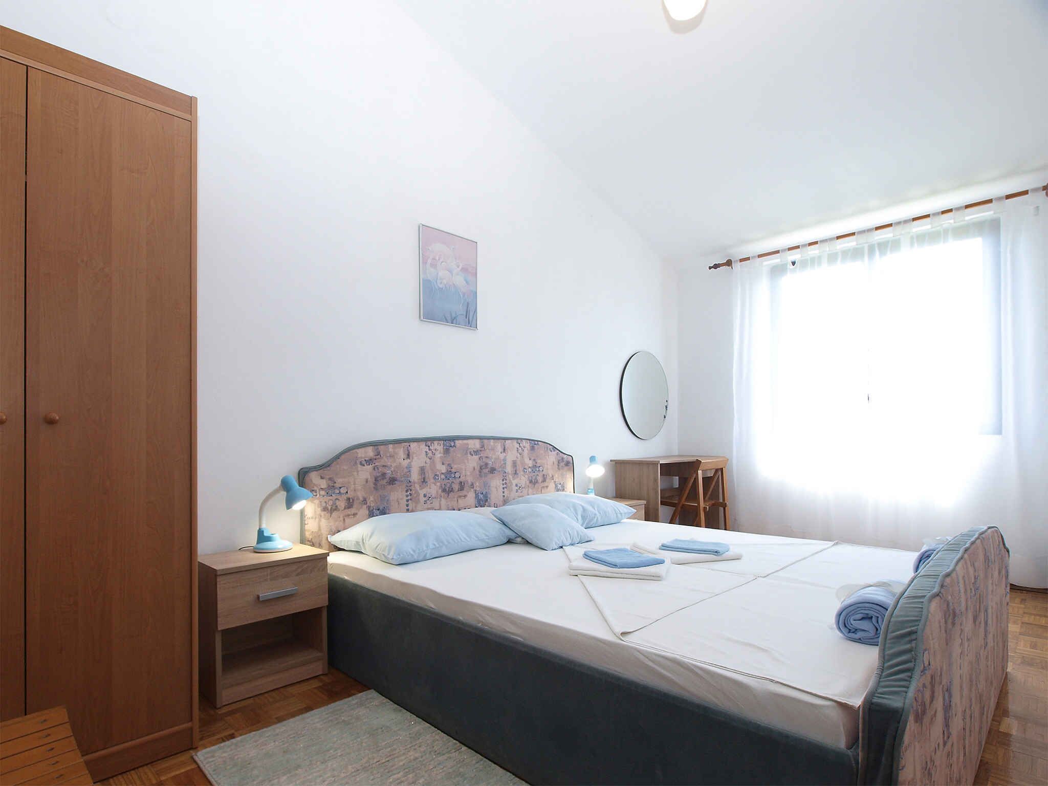 A bedroom with a bed, a nightstand, a wardrobe, a mirror, and a window with curtains.