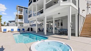 En moderne bygning med flere etager, pool, jacuzzi, udendørs siddepladser og en overdækket terrasse.