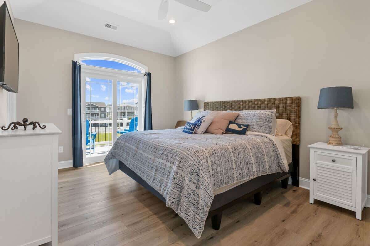 A bedroom with a bed, nightstands, a lamp, a ceiling fan, and a view through a glass door.