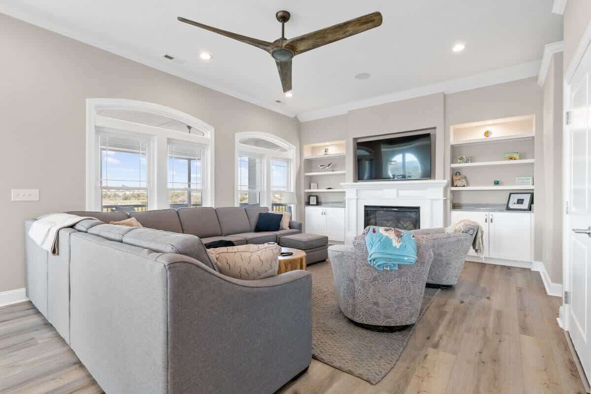 A spacious living room with a large sofa, a smaller armchair, a fireplace, and a ceiling fan.