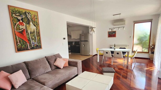 A modern living room with a sofa, coffee table, and a dining area with chairs and a table.