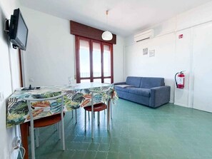 Una habitación con una mesa de comedor, sillas, un sofá, un televisor y un extintor.